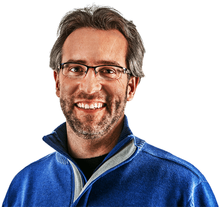 Man with gray hair and beard wearing glasses and blue shirt is smiling